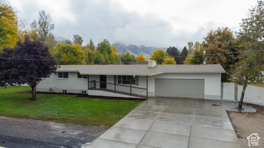 Single-level ranch-style home featuring painted brick siding, an attached two-car garage, concrete driveway, and a covered front porch with metal railing