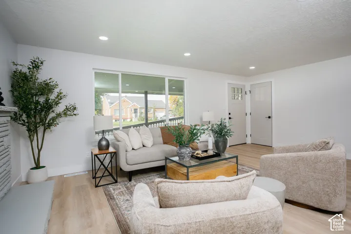 Living area featuring wood-finish flooring, recessed lighting, a large picture window, a textured stone fireplace surround, and a paneled entry door