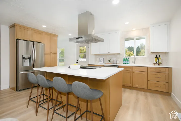 Kitchen featuring two-tone cabinetry, a central island with a quartz countertop, stainless steel appliances, a ceiling-mounted range hood, and light-toned wood-finish flooring