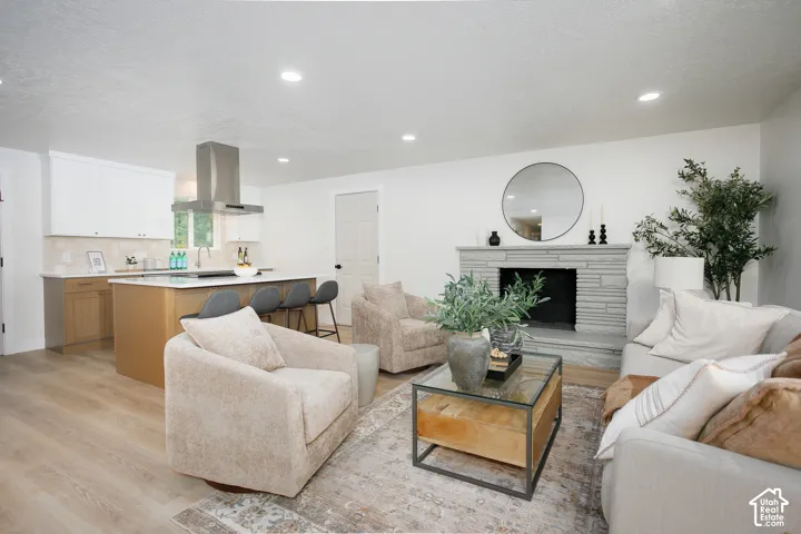 Open-concept living space featuring wood-finish flooring, recessed lighting, a stone-surround fireplace, and a kitchen equipped with a center island and stainless steel range hood