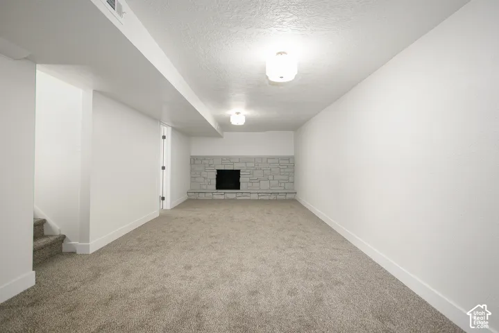 Neutral-toned interior space featuring stone-surround fireplace, textured carpet flooring, and dual flush-mount ceiling fixtures