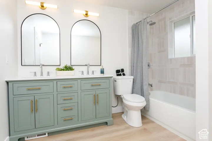 Dual-sink vanity with sage green cabinetry and gold-tone hardware, arched mirrors, wall-mounted light fixtures, and a tub-shower combination featuring textured tile surround