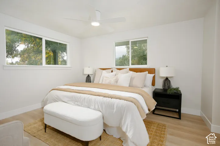 Neutral interior featuring light-tone wood-finish flooring, dual sliding windows, and a central ceiling fan with an integrated light fixture
