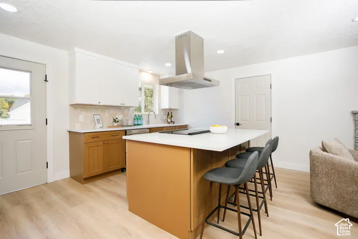 Kitchen featuring two-tone cabinetry, central island with quartz countertop, stainless steel vent hood, and light-toned wood-finish flooring
