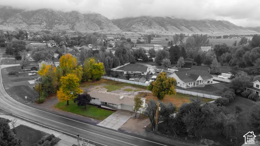 Aerial perspective of a single-story residence featuring an attached garage, a concrete driveway, mature trees, and a mountain backdrop