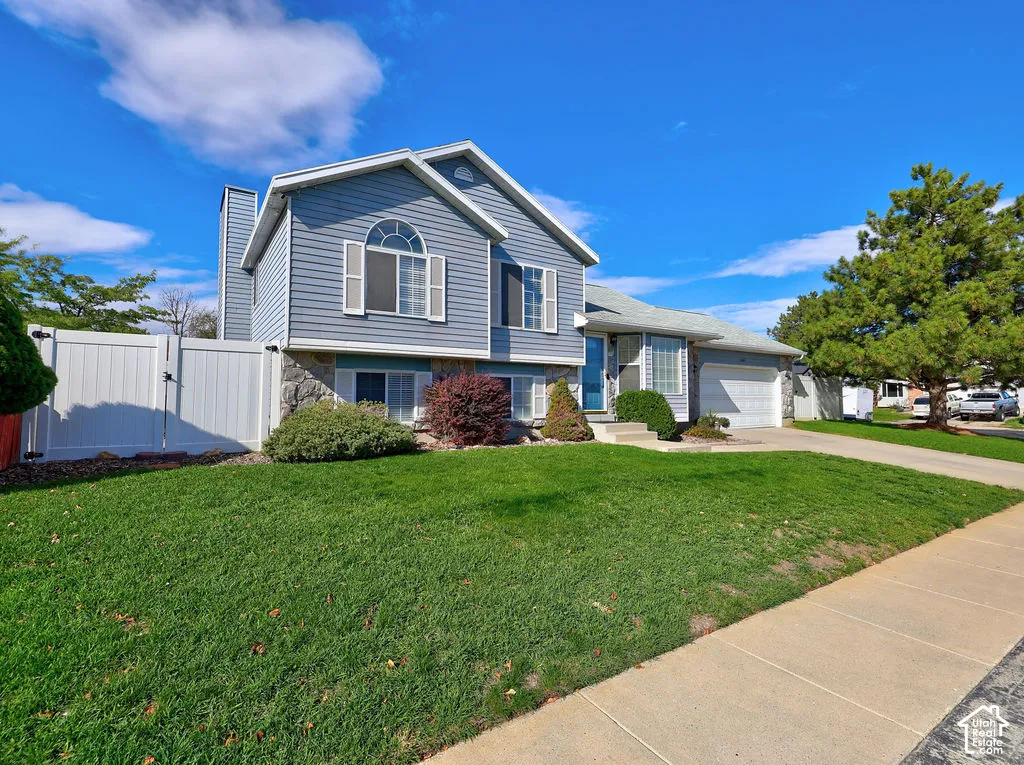 Split-level exterior featuring horizontal siding, stone veneer accents, arched window detailing, an attached two-car garage, and a solid white privacy fence