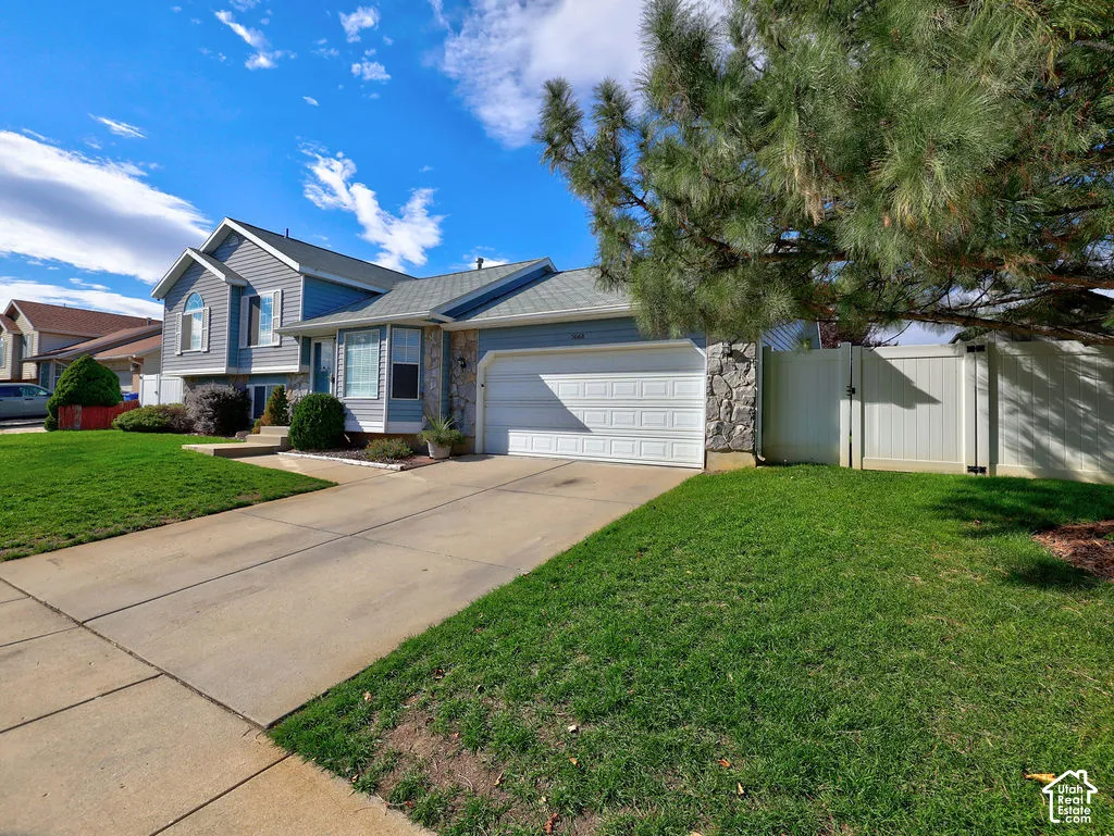 Multi-level exterior featuring horizontal lap siding, stone veneer accents, concrete driveway, attached two-car garage, and solid vinyl privacy fencing