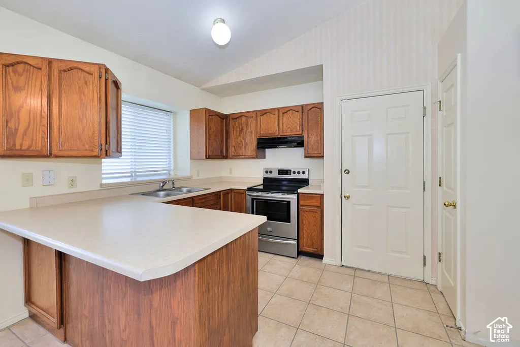 Kitchen featuring wood cabinetry, stainless steel range, solid-surface countertops, dual-basin stainless steel sink, and tile flooring