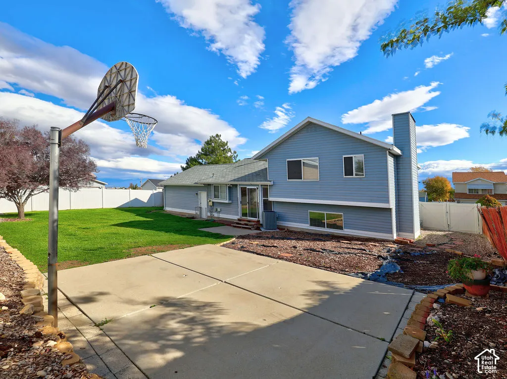 Rear exterior featuring horizontal lap siding, an expansive concrete patio, a dedicated sports court area with a fixed basketball hoop, a manicured lawn, and natural stone border retaining walls