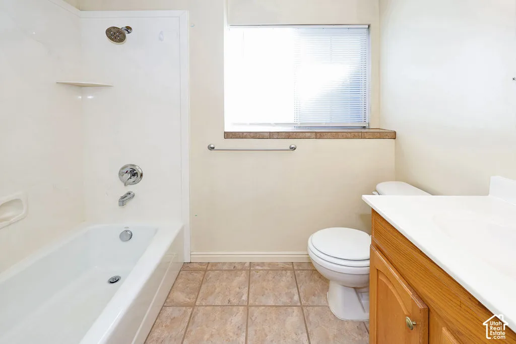 Full bathtub with integrated surround, wood-finish vanity with countertop basin, tile flooring, and window with built-in tile sill