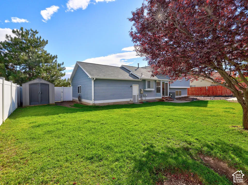 Backyard featuring a manicured lawn, vinyl privacy fencing, mature landscaping, and a detached storage shed
