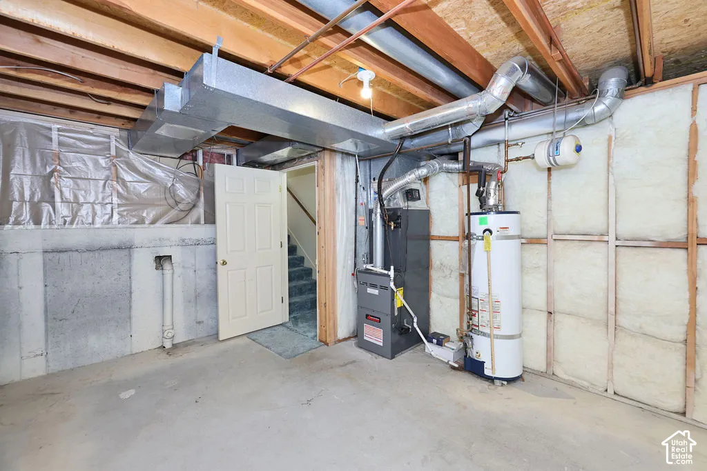 Utility area featuring exposed joist ceiling, concrete flooring, furnace, water heater, and fiberglass wall insulation