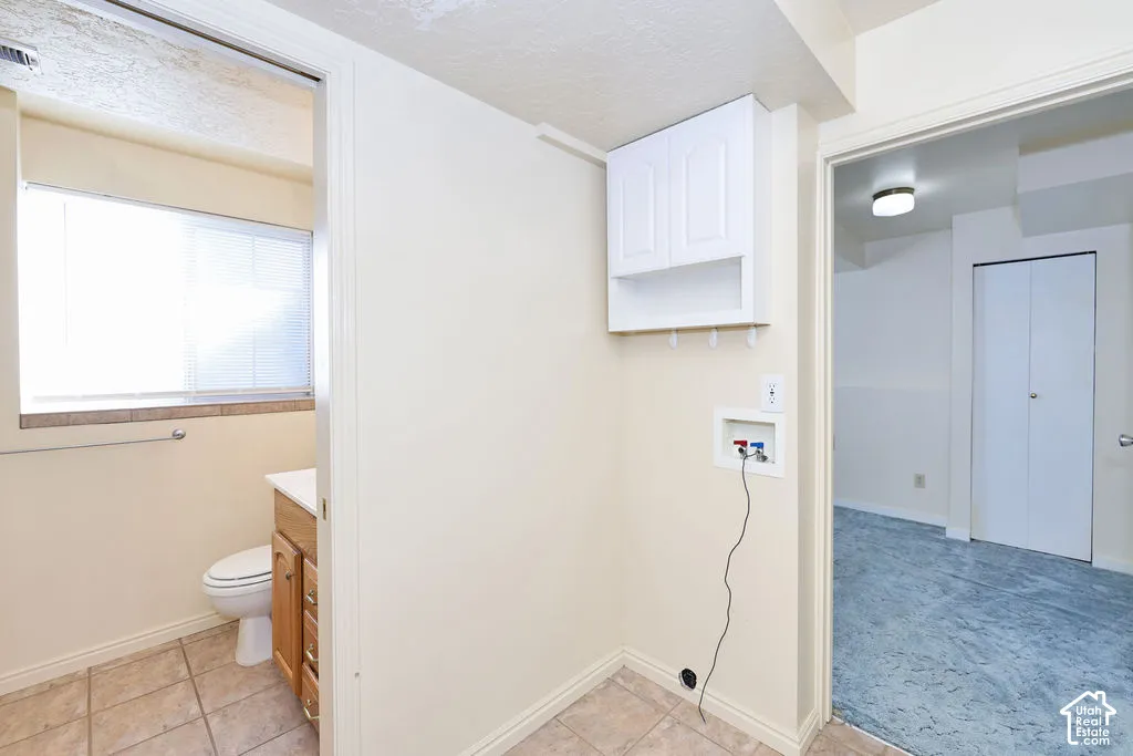 Laundry area featuring wall-mounted upper cabinetry, tile flooring, and utility hookups, with a restroom containing a wood-finish vanity and tile flooring, and a separate space with a dual-door closet