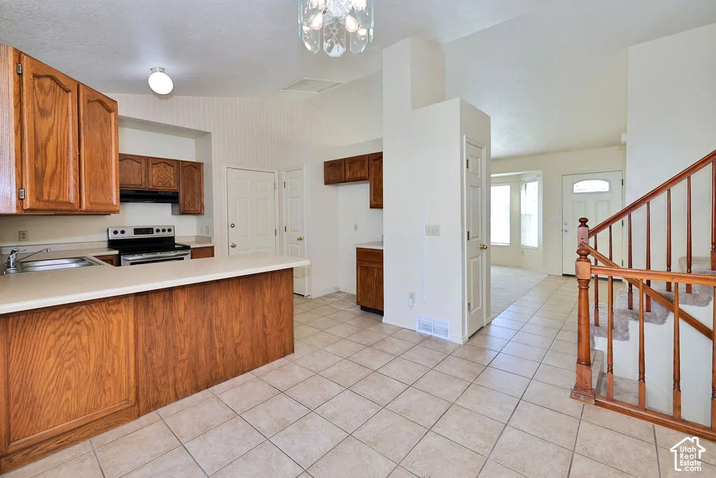 Kitchen featuring stained wood cabinetry, a peninsula counter, tile flooring, vaulted ceilings, and a wooden stair railing