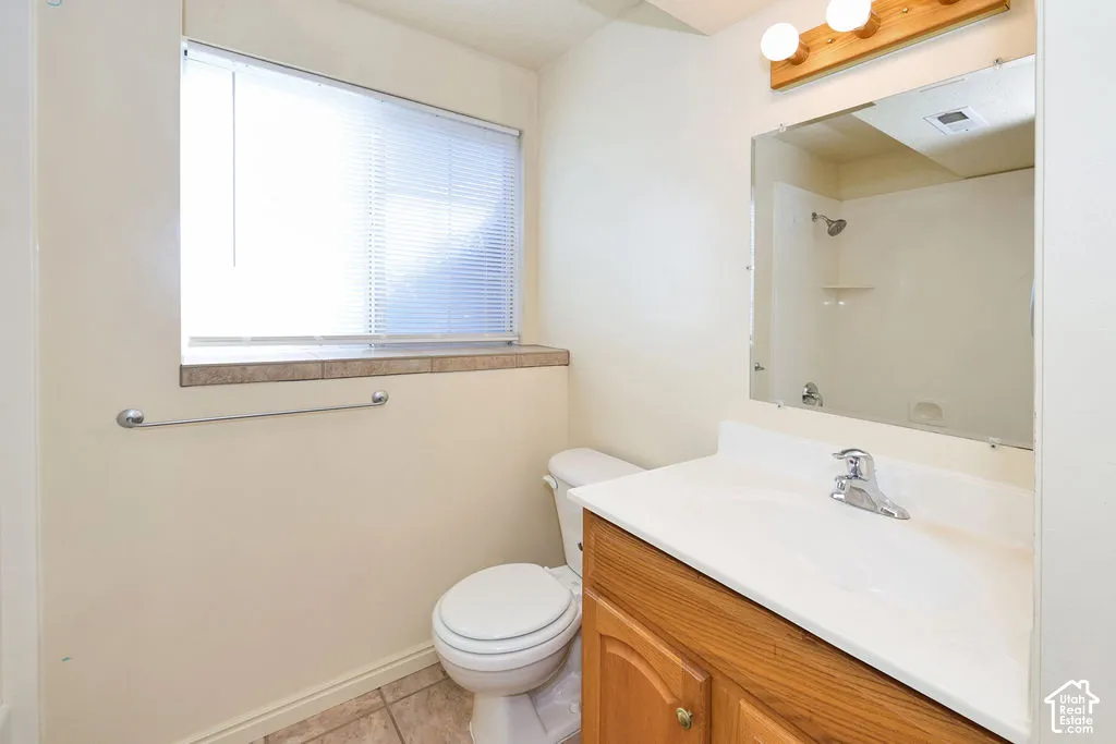 Wood-finish vanity with a white countertop and integrated sink, large wall-mounted mirror, three-light fixture, and ceramic tile flooring