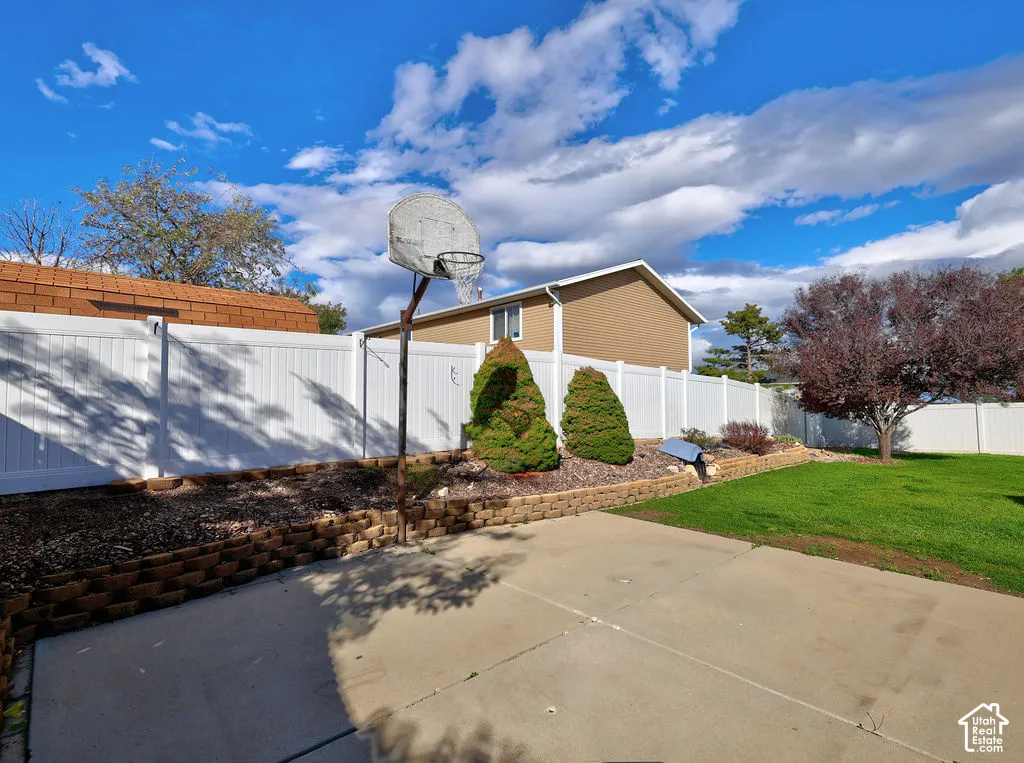 Private backyard featuring a concrete patio, tiered stone retaining walls, white vinyl privacy fencing, and mature landscaping