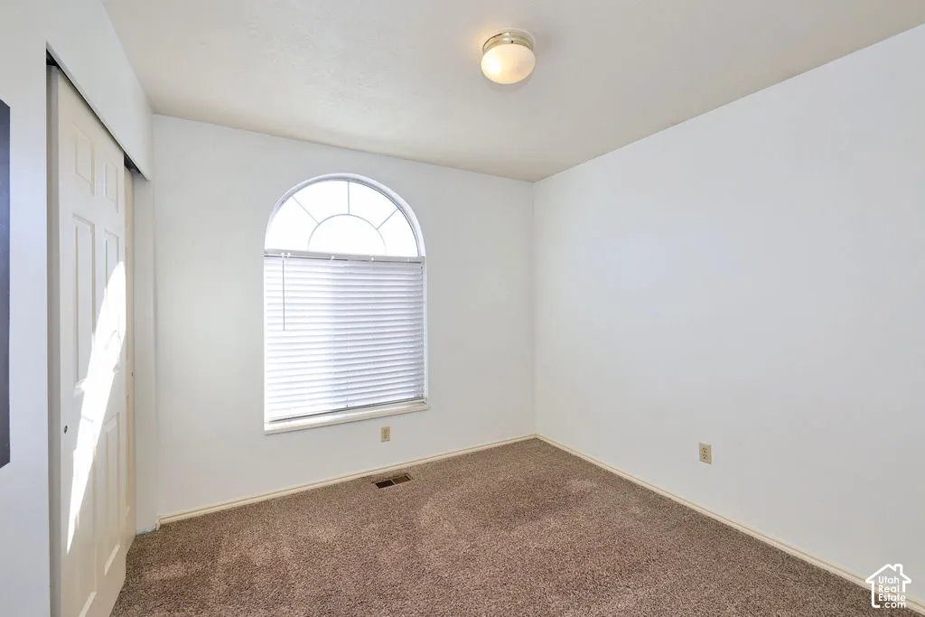 Neutral-toned carpeting, arched window with decorative muntins, flush-mount ceiling light fixture, and double-panel sliding closet doors