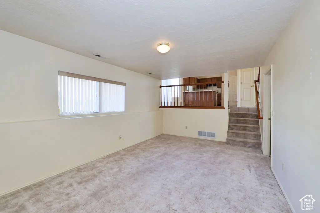 Carpeted interior space featuring a multi-level layout, wooden stair railing, and a window with integrated vertical blinds