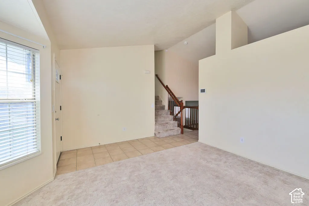 Neutral-toned interior featuring ceramic tile flooring at the entryway, carpeted flooring in the main space, vaulted ceilings, and a staircase with a wood-finish handrail and balusters