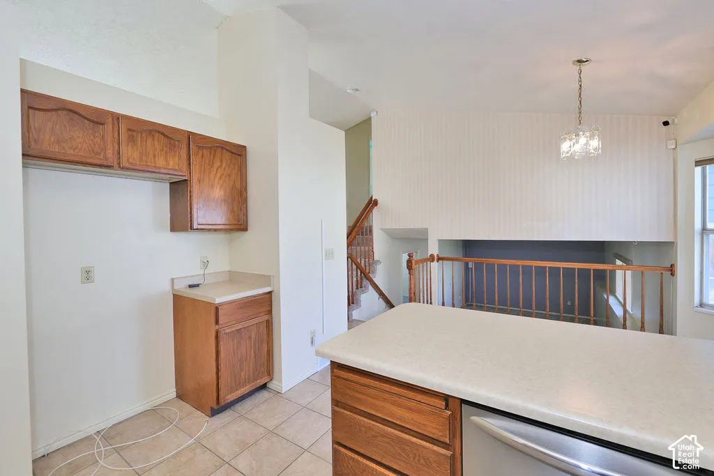 Kitchen area featuring wood cabinetry, solid-surface countertops, tile flooring, vaulted ceilings, and a decorative pendant light fixture