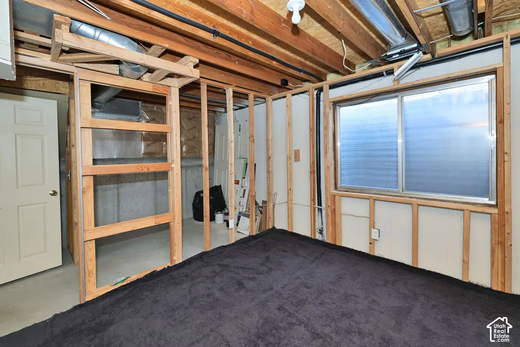 Unfinished room featuring exposed wood framing, concrete foundation walls, a sliding window, and a paneled interior door