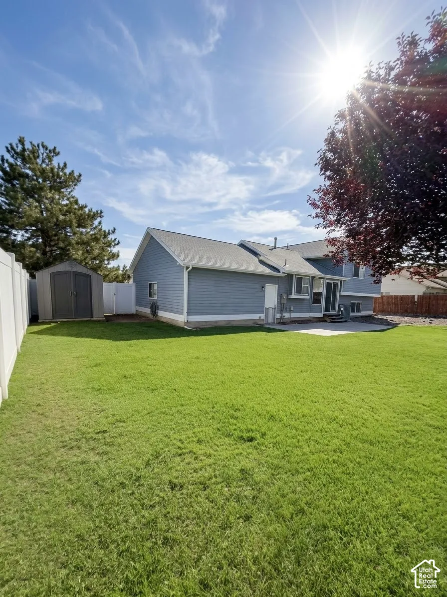 Expansive backyard featuring a manicured lawn, white vinyl perimeter fencing, detached storage shed, and concrete patio