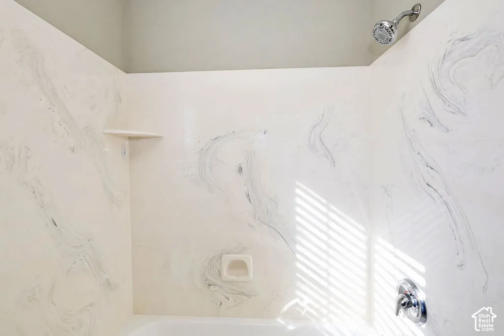 Shower and bathtub surround featuring a white-and-grey marbled pattern finish, integrated corner shelf, built-in recessed soap dish, and chrome-finished plumbing fixtures