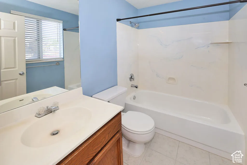 Bathroom featuring a vanity with a solid-surface countertop, an integrated sink, a combination shower and tub with a surround, and tile flooring