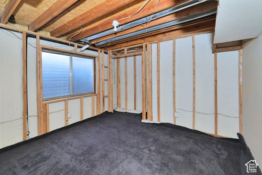 Unfinished space featuring exposed wood-frame wall studs, exposed ceiling joists, grey carpeting, and a sliding window