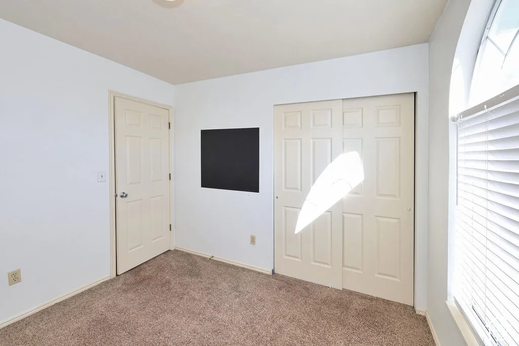 Room featuring neutral wall-to-wall carpeting, a six-panel closet door, a single-panel interior door, and an arched window with horizontal blinds