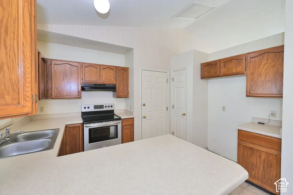 Kitchen featuring vaulted ceilings, wood-finish cabinetry, neutral solid-surface countertops, dual-basin stainless steel sink, and stainless steel freestanding range