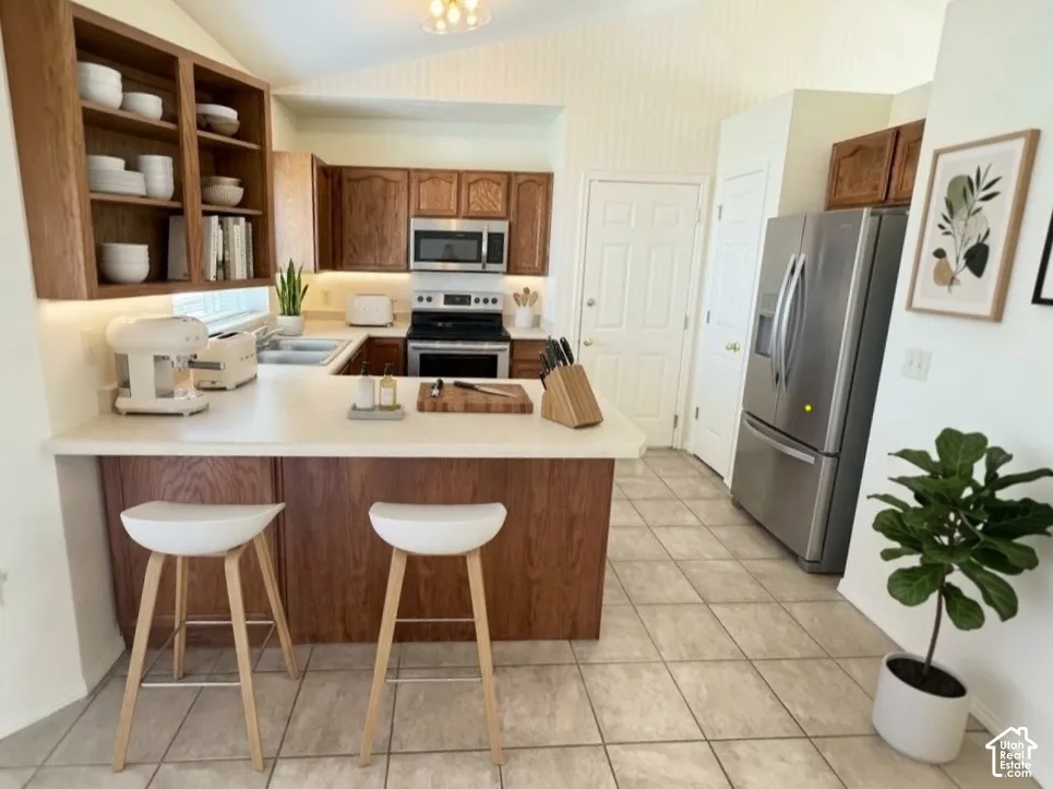 Kitchen featuring stained-wood cabinetry, open shelving, stainless steel appliances, solid-surface countertops, and vaulted ceilings