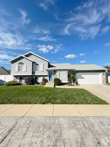 Split-level exterior featuring light gray horizontal siding, stone veneer accents, an arched window, a concrete driveway, and an attached two-car garage