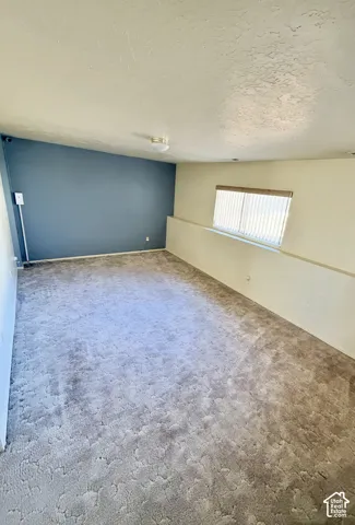 Interior space featuring wall-to-wall carpeting, slanted ceiling, contrasting accent wall, and recessed window with vertical blinds