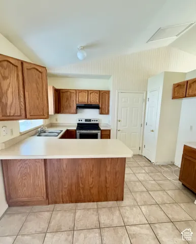 Kitchen featuring natural-finish wood cabinetry, a peninsula countertop, tile flooring, a stainless steel range, and vaulted ceilings