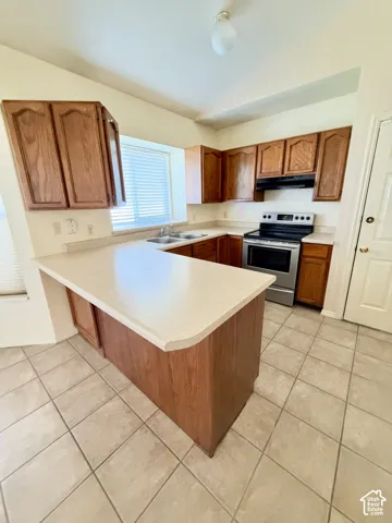 Kitchen featuring solid-surface countertops, wood cabinetry, a stainless steel electric range, a dual-basin sink, and tile flooring