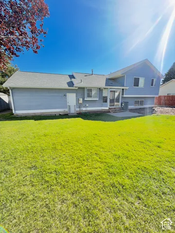 Exterior featuring light blue lap siding, a gray shingle roof, concrete patio, and an expansive lawn