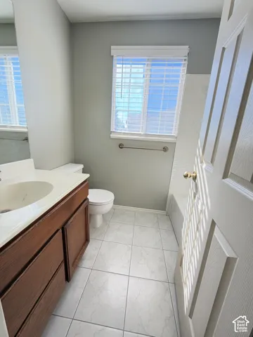 Bathroom featuring a wood-finish vanity, integrated countertop with sink, tiled flooring, horizontal blinds, and a built-in tub shower