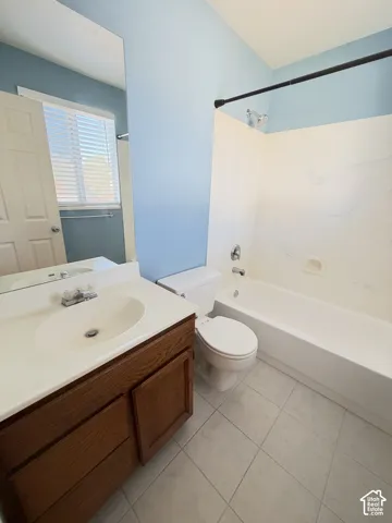 Full bathroom featuring a wood-finish vanity, solid-surface countertop with an integrated sink, porcelain tile flooring, and a tub-shower combination with a surround