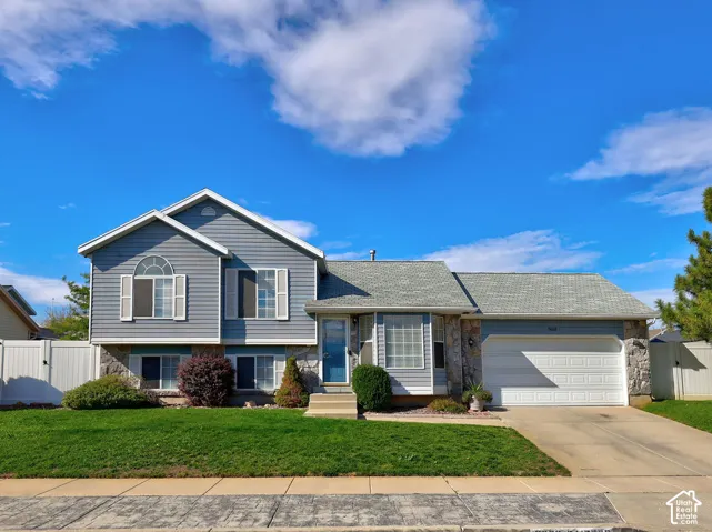 Multi-level residence featuring horizontal lap siding, stone veneer accents, an arched window, a two-car garage, and a concrete driveway