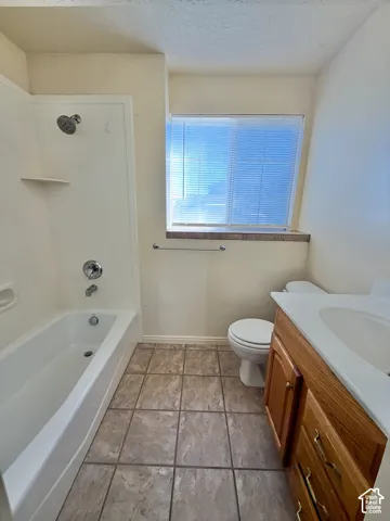 Bathroom featuring a tub-shower combination with chrome fixtures, wood-finish cabinetry with a white vanity top, and square ceramic floor tile