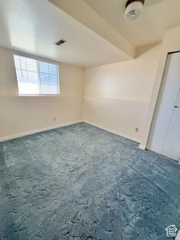 Room featuring wall-to-wall carpeting, a window with horizontal blinds, neutral wall paint, a ceiling-mounted light fixture, and a closet with bifold doors