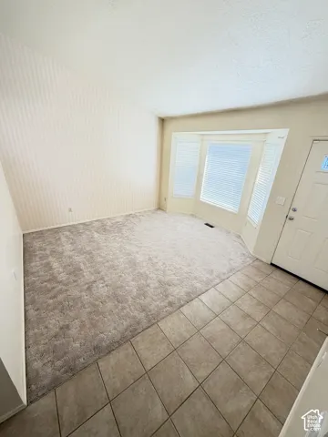 Vaulted ceilings, bay window with integrated blinds, wall-to-wall carpeting, and neutral tile flooring