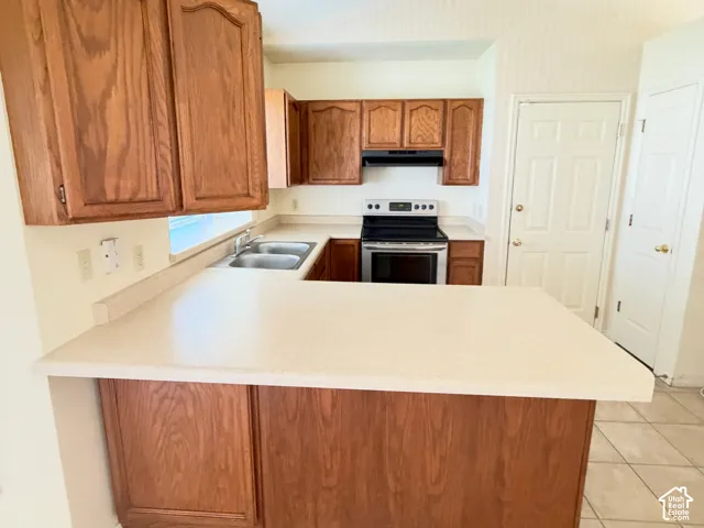 Kitchen featuring wood cabinetry, a peninsula with a solid-surface countertop, tile flooring, and integrated range