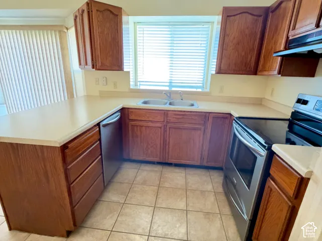 Kitchen featuring wood cabinetry, solid-surface countertops, tile flooring, stainless steel appliances, and a double-basin sink