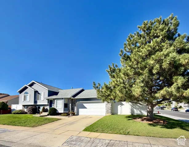 Split-level exterior featuring horizontal siding, stone veneer accents, an attached two-car garage, and a mature evergreen tree