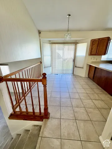 Vaulted ceiling, tile flooring, wooden railing with turned balusters, sliding glass door with integrated blinds, and wood-finish cabinetry