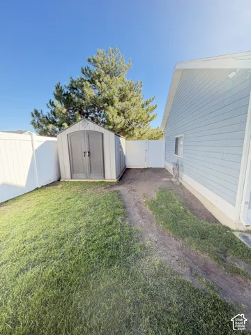 Exterior side yard featuring light blue horizontal siding, a white vinyl privacy fence, and a neutral-toned storage shed