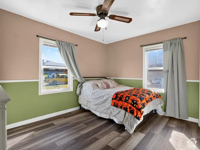 Wood-finish flooring, two large windows with natural light, and a central ceiling fan with integrated lighting