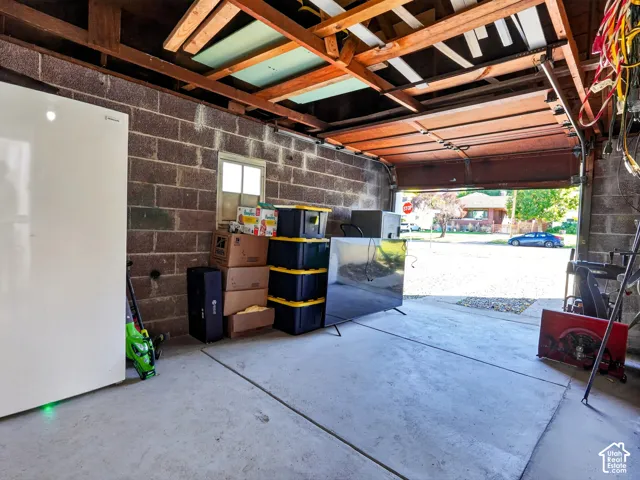 Garage featuring exposed ceiling joists, concrete flooring, and masonry block walls with a fixed-pane window